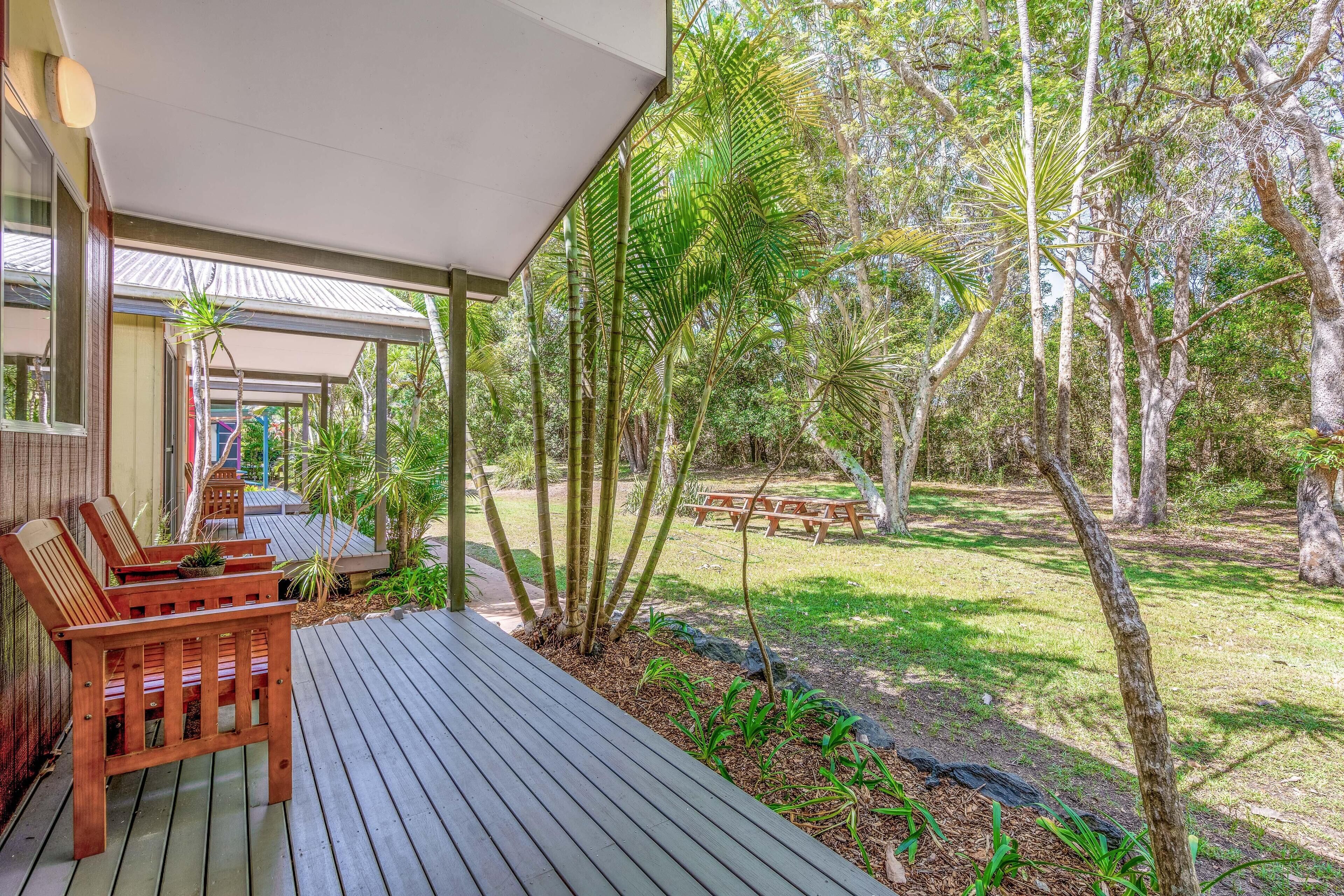 A wooden deck with a covered seating area, surrounded by a garden with various plants and trees.