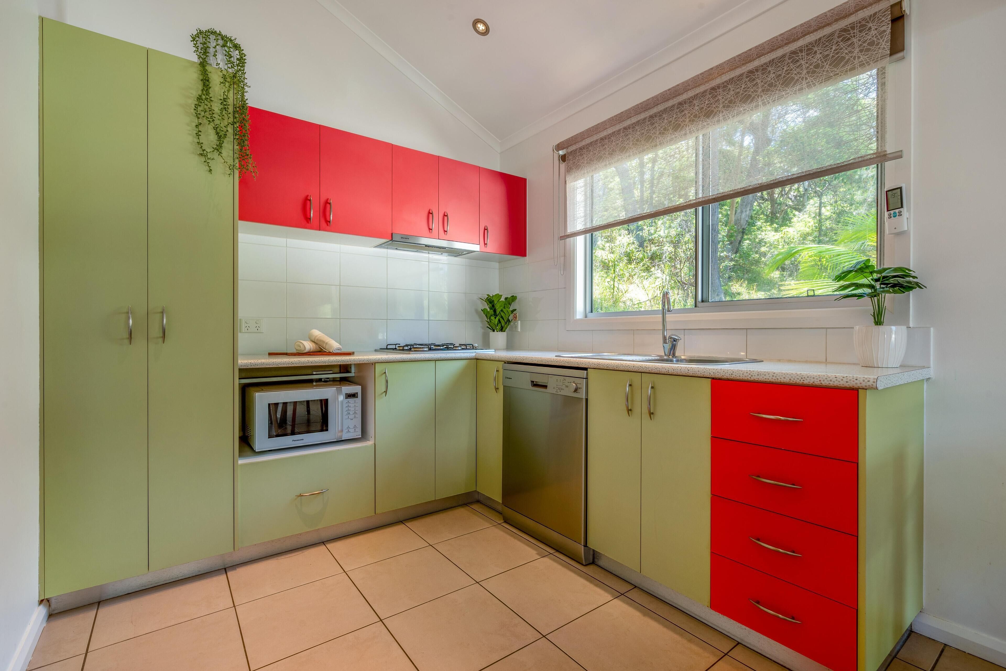 A kitchen with green and red cabinets, a window with a view of greenery, a built-in oven, and a dishwasher.