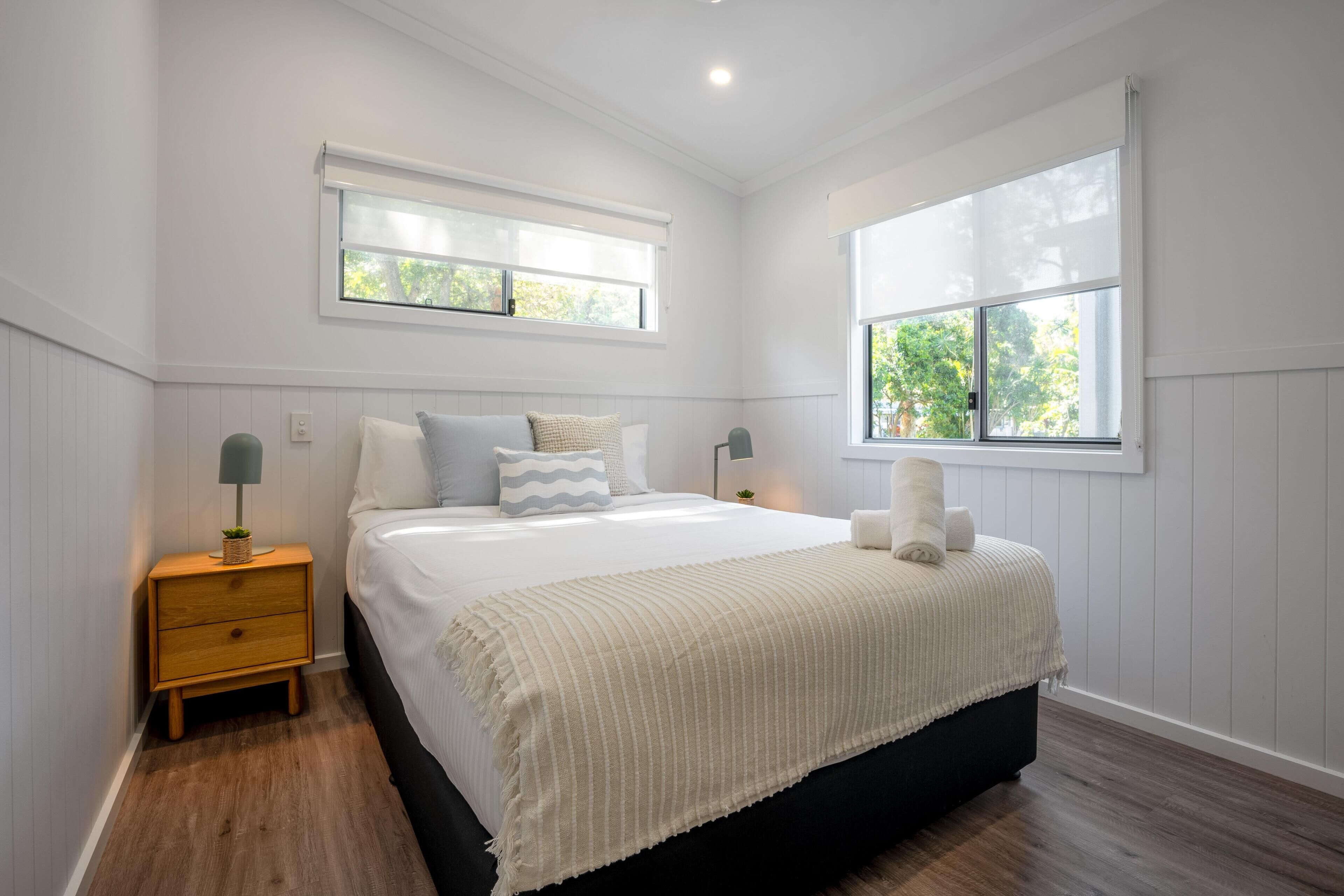 A bedroom with a large bed, two bedside tables, a window, and a view of trees.