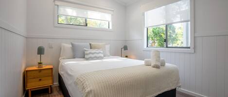 A bedroom with a large bed, two bedside tables, a window, and a view of trees.