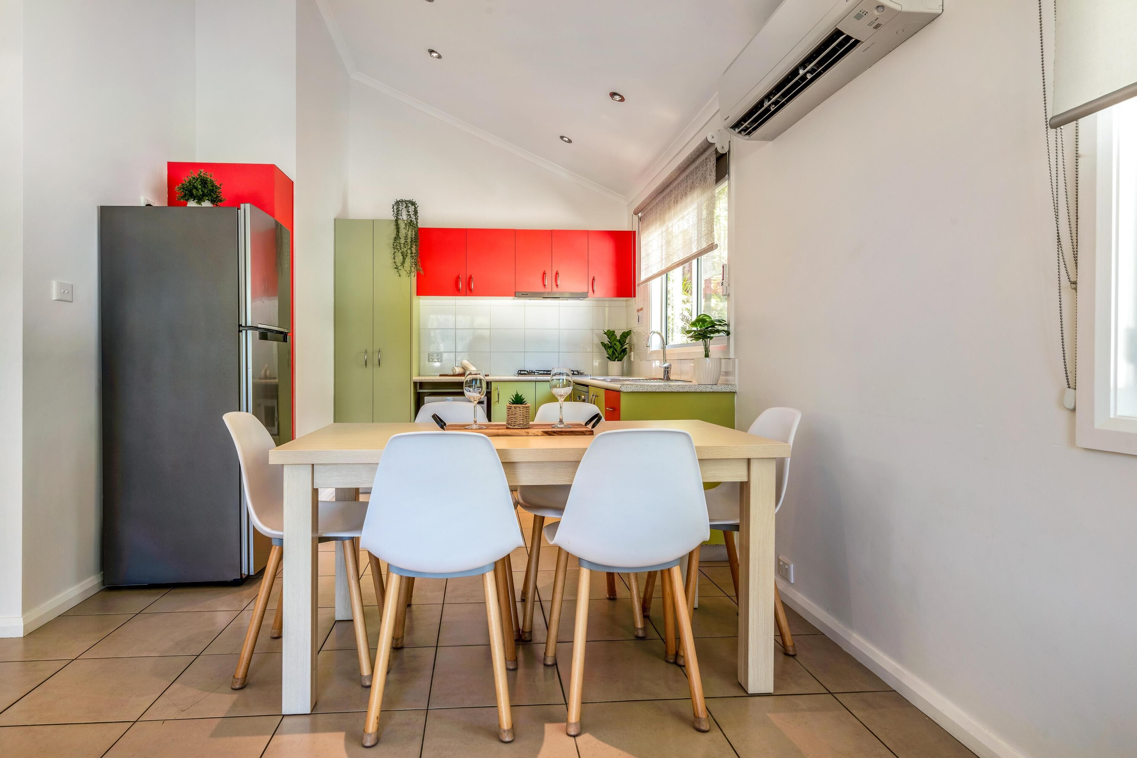 A modern kitchen with a dining area, featuring a stainless steel refrigerator, a wooden table with four chairs, and red and green cabinets.
