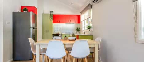 A modern kitchen with a dining area, featuring a stainless steel refrigerator, a wooden table with four chairs, and red and green cabinets.