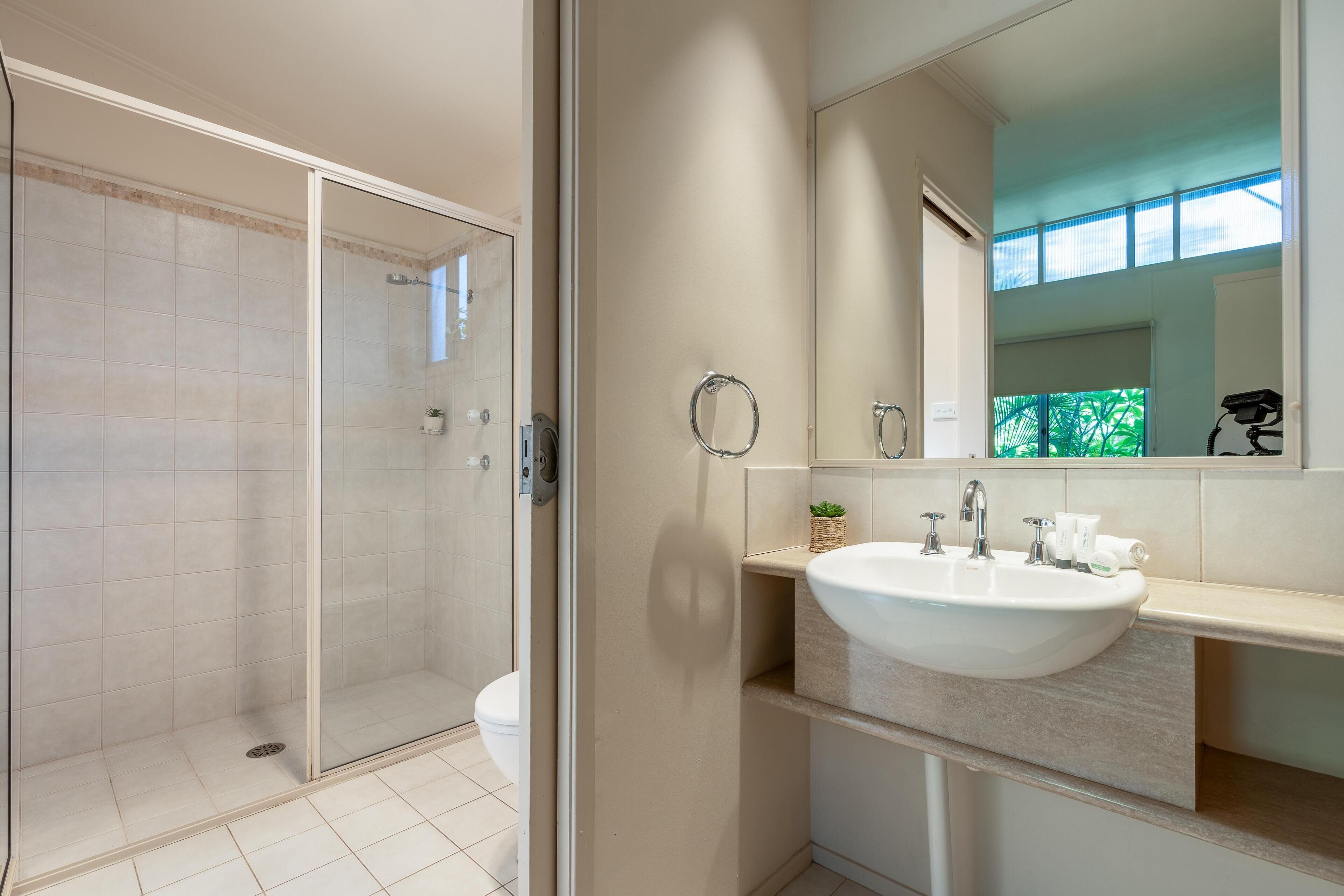 A modern bathroom with a glass shower enclosure, a white sink, and a large mirror.