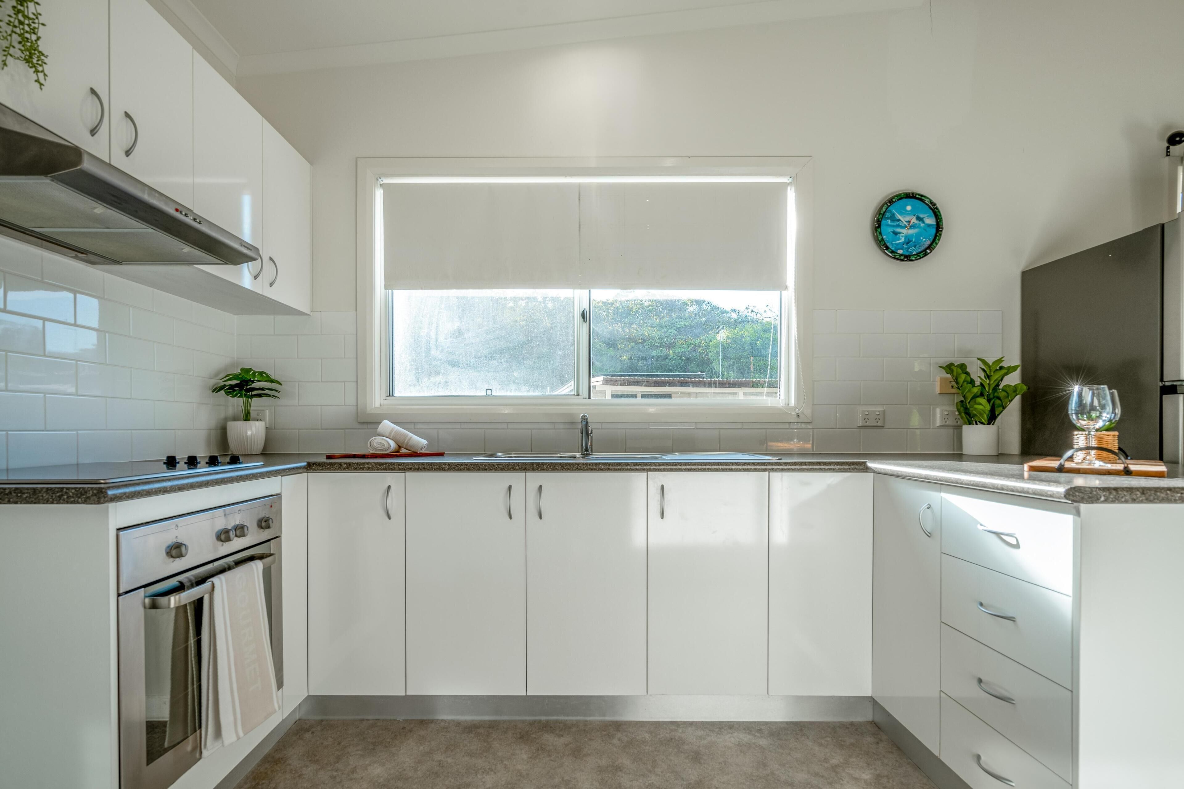 A modern kitchen with white cabinets, a stainless steel oven, a window with a view, and a potted plant on the counter.