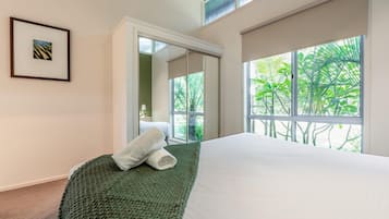 Habitación de hotel con una cama grande, una manta verde, un cuadro en la pared y vistas a la vegetación por la ventana.