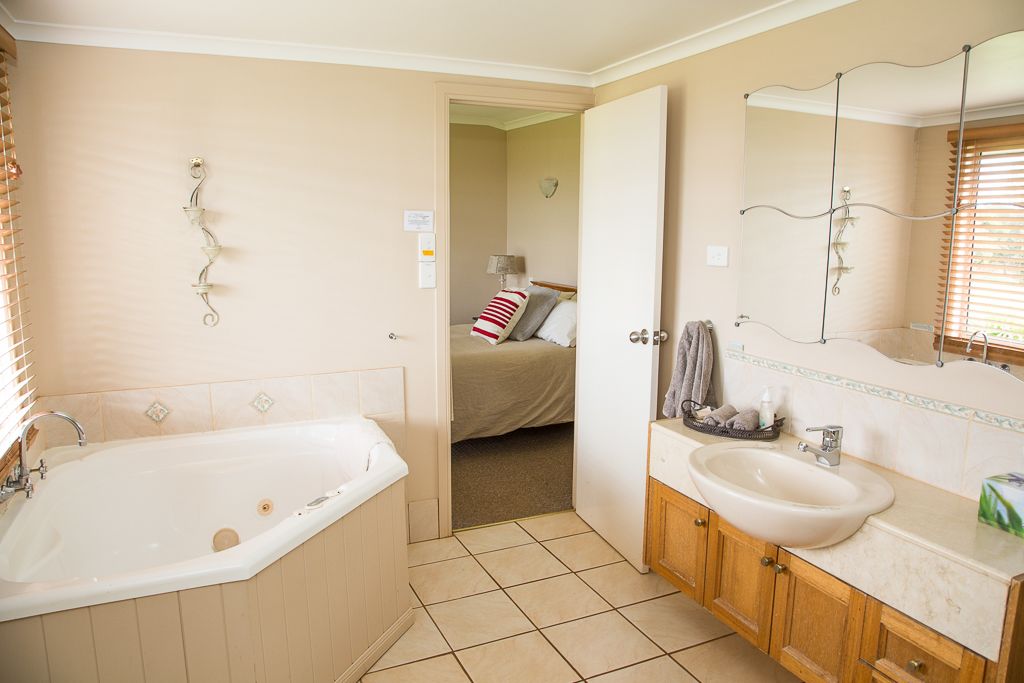 Un bagno con vasca, lavabo e specchio. Si intravede un letto nella stanza adiacente.