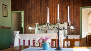 Una mesa de comedor de madera con una taza azul y flores rosas, un candelabro con tres velas y un mantel blanco.