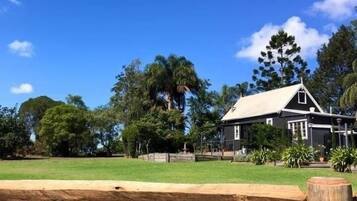 A house with a white roof and dark siding, surrounded by a grassy lawn and trees.