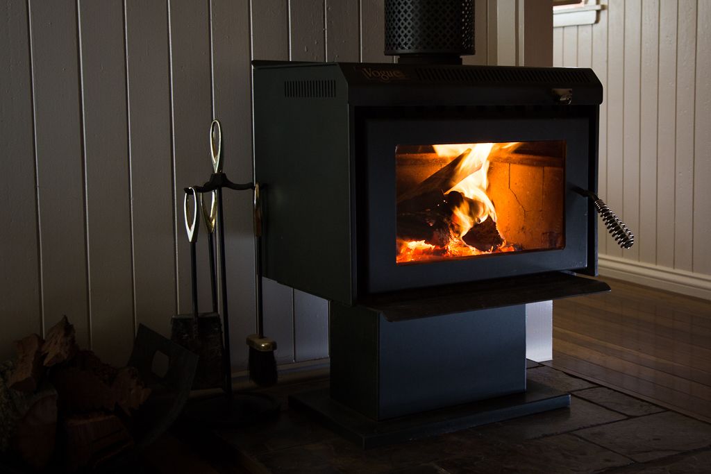 A wood-burning stove with a visible fire, a metal stand, and logs beside it.
