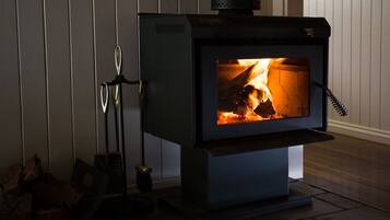 Ein Kaminofen mit sichtbarem Feuer, einem Metallständer und Holzscheiten daneben.