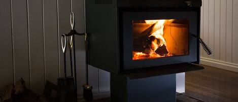 A wood-burning stove with a visible fire, a metal stand, and logs beside it.