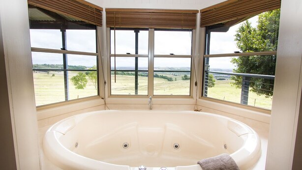 Un baño en esquina con una bañera grande, tres ventanas y vistas a un paisaje verde.