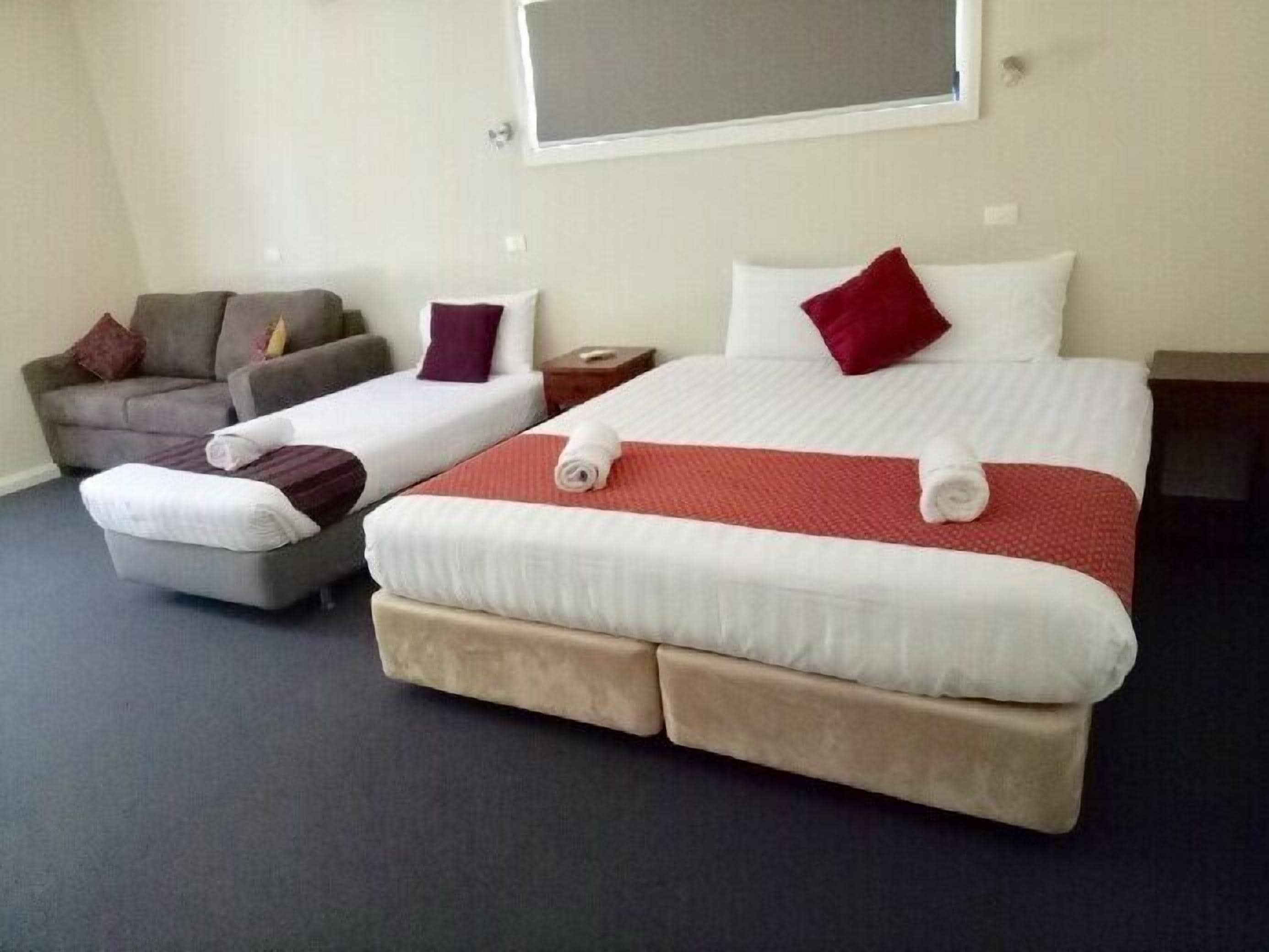 Hotellihuone, jossa on suuri sänky, kaksi pienempää sänkyä, sohva ja yöpöytä.