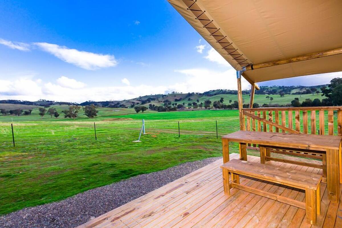 A wooden deck with a bench overlooking a green field.