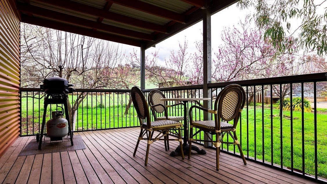 A covered outdoor deck with a grill, chairs, and a view of a green lawn and trees.