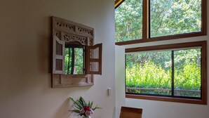 Ein Essbereich mit Holztisch, Stühlen, einer Vase mit Blumen, einem dekorativen Spiegel und großen Fenstern mit Blick auf Grünflächen.