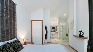 A bedroom with a bed, a bedside table, a nightstand, a mirror, and a door leading to a bathroom. - Limpinwood Lodge (Limpinwood)