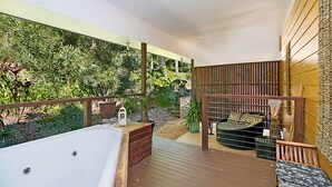 Ein modernes Badezimmer im Freien mit Whirlpool, Holzterrasse und Blick auf üppige Vegetation.