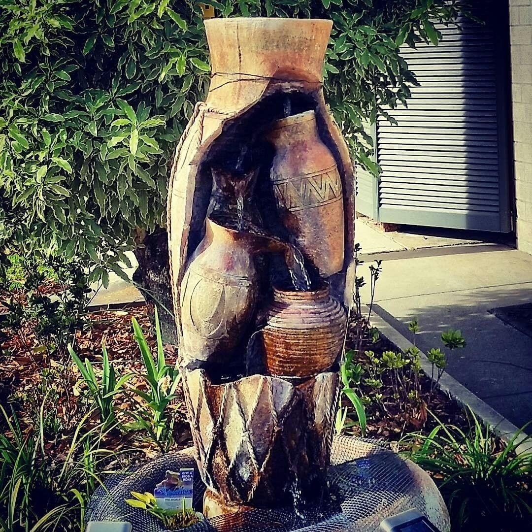 Escultura d'una figura humana dins una estructura semblant a un vas, situada a l'aire lliure amb un jardí i un edifici al fons.