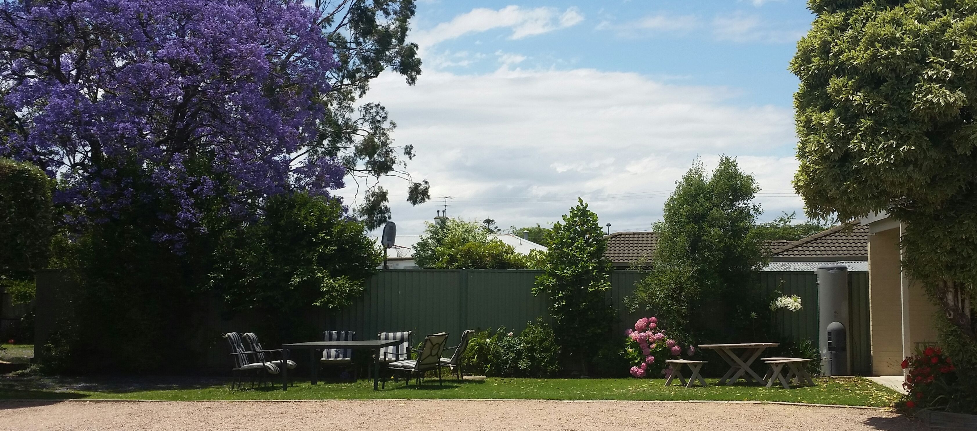 Un patio con mobiliario exterior, una cerca verde y un edificio al fondo.