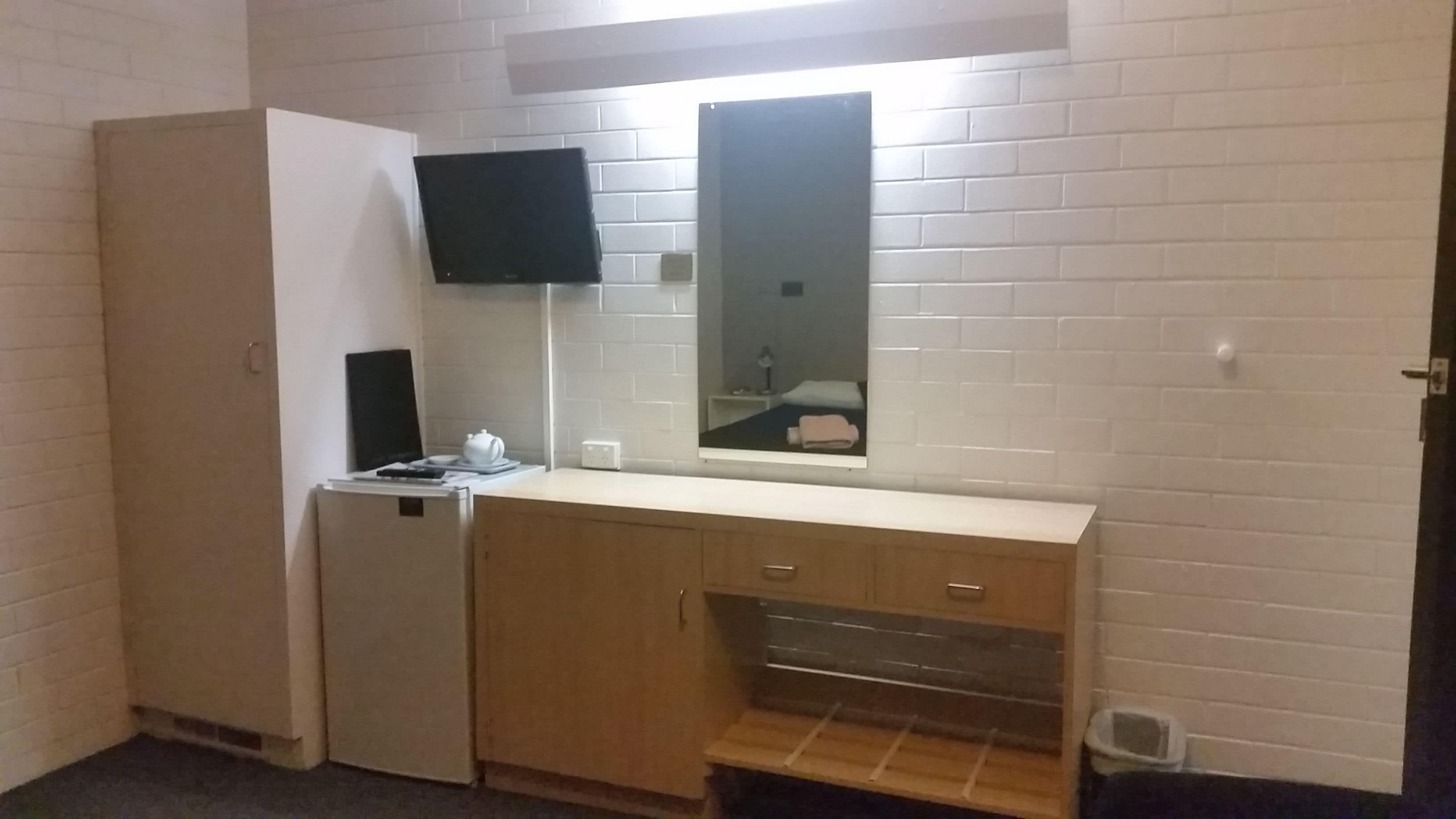 Una habitación pequeña y compacta con kitchenette, un televisor de pantalla plana sobre la encimera y un espejo que refleja parte de la habitación.