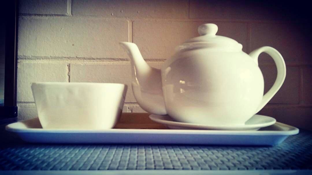 A white teapot and cup on a tray.