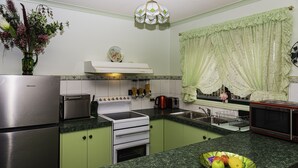 Una cocina con armarios verdes, un refrigerador de acero inoxidable, un microondas y un lavamanos.