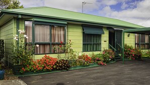Un edificio verde con varias ventanas, una puerta y un pequeño jardín con diversas flores.