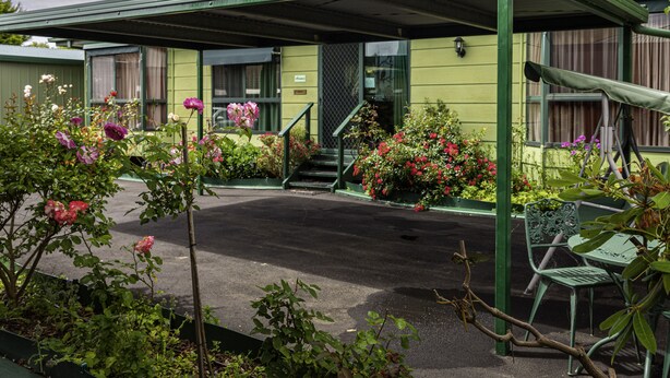 Un edificio verde con un acceso cubierto, una escalera y un banco.