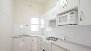 Una cocina con armarios blancos, estufa a gas, microondas y ventana.