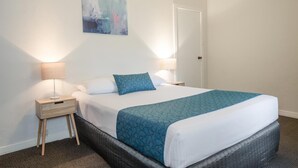 Habitación de hotel con cama, dos lámparas de noche, una mesita auxiliar, una obra de arte en la pared y una puerta.