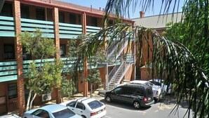 Un edificio de varios pisos con fachada de ladrillo, toldo verde y escape de incendios visible. Hay coches estacionados frente al edificio.