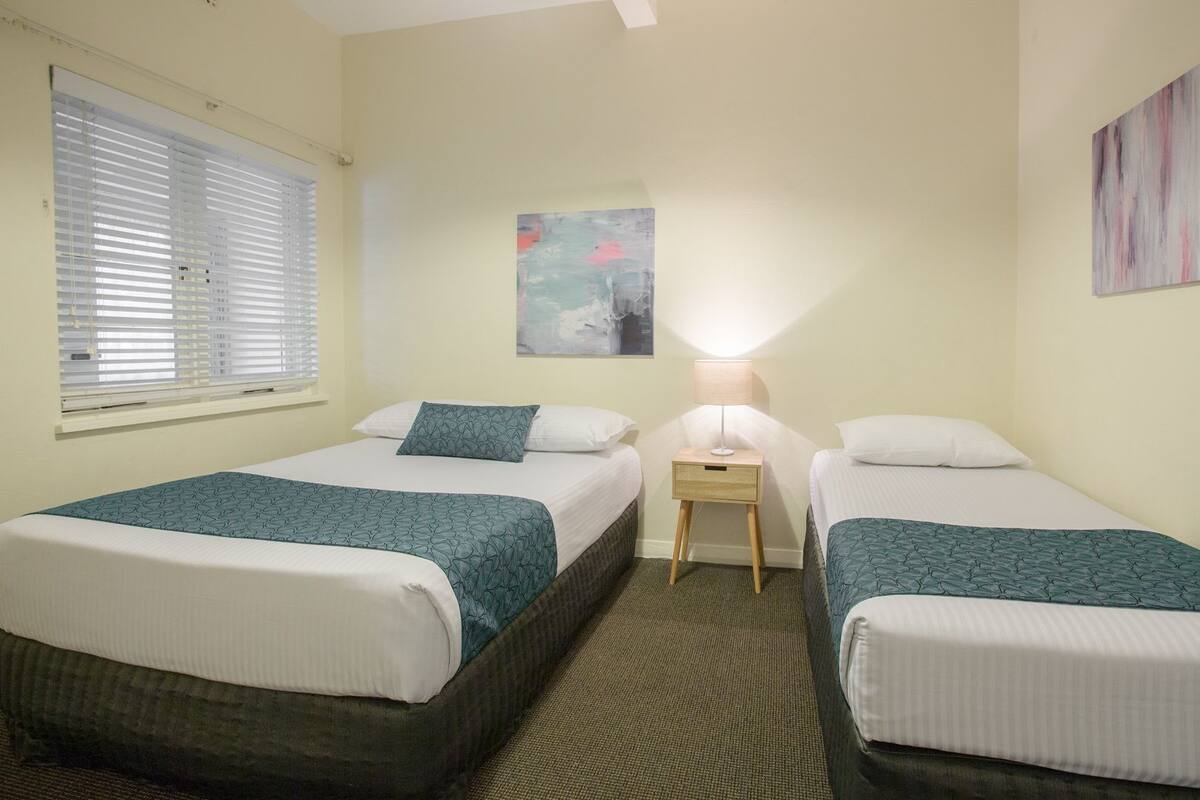 Una habitación de hotel con dos camas, una mesita de noche, una lámpara y un cuadro en la pared.