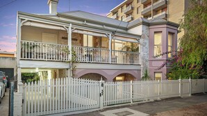 Un bâtiment à deux étages doté d’un balcon, d’une clôture blanche en bois et d’une façade en briques.