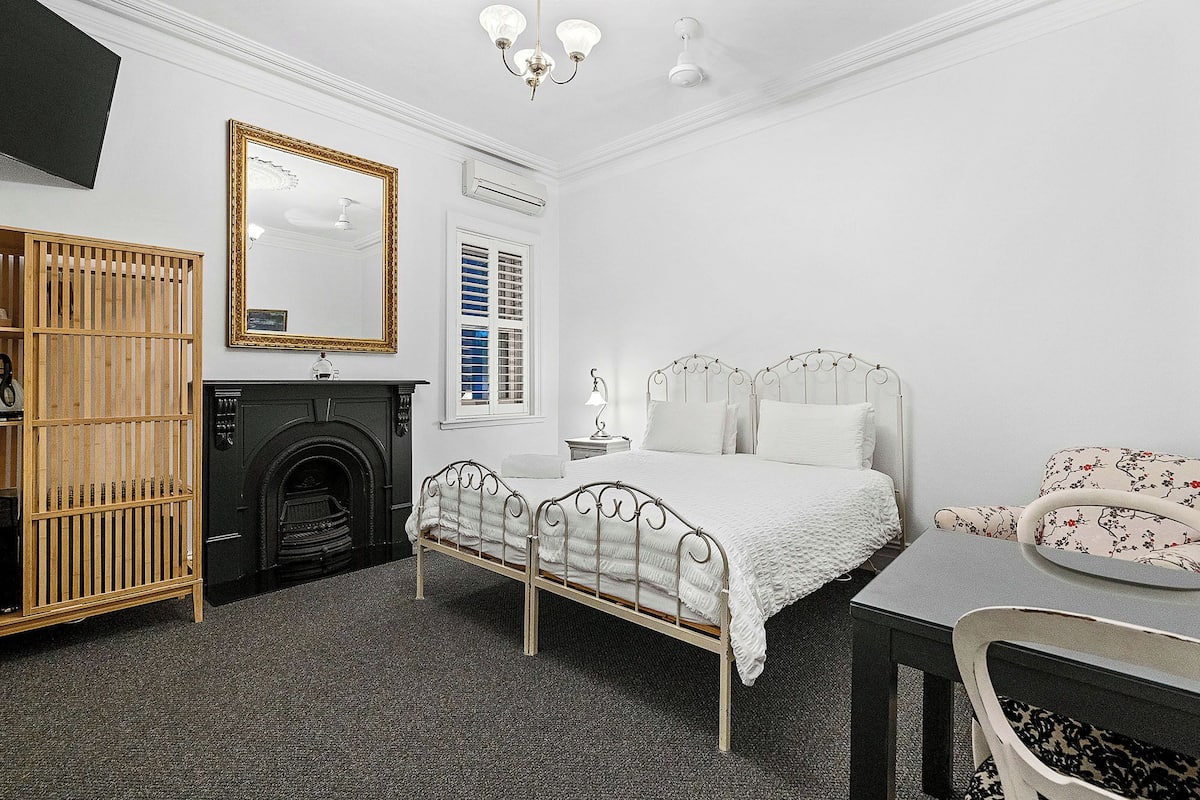 A bedroom with a bed, a dresser, a mirror, a fireplace, and a window with shutters.