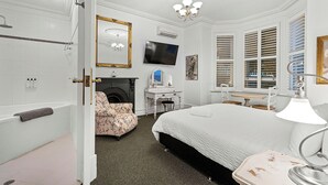 Une chambre à coucher comprenant un lit, une commode, un miroir, un téléviseur et une cheminée.