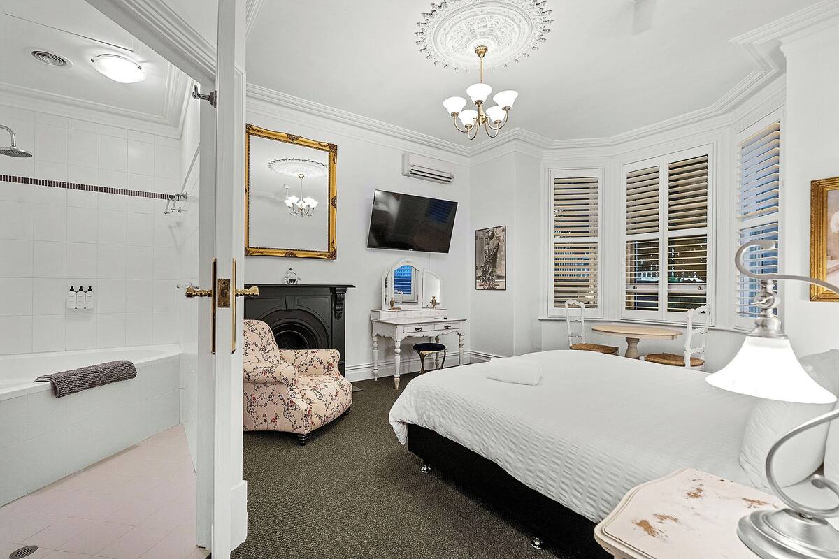 A bedroom with a bed, a dresser, a mirror, a television, and a fireplace.