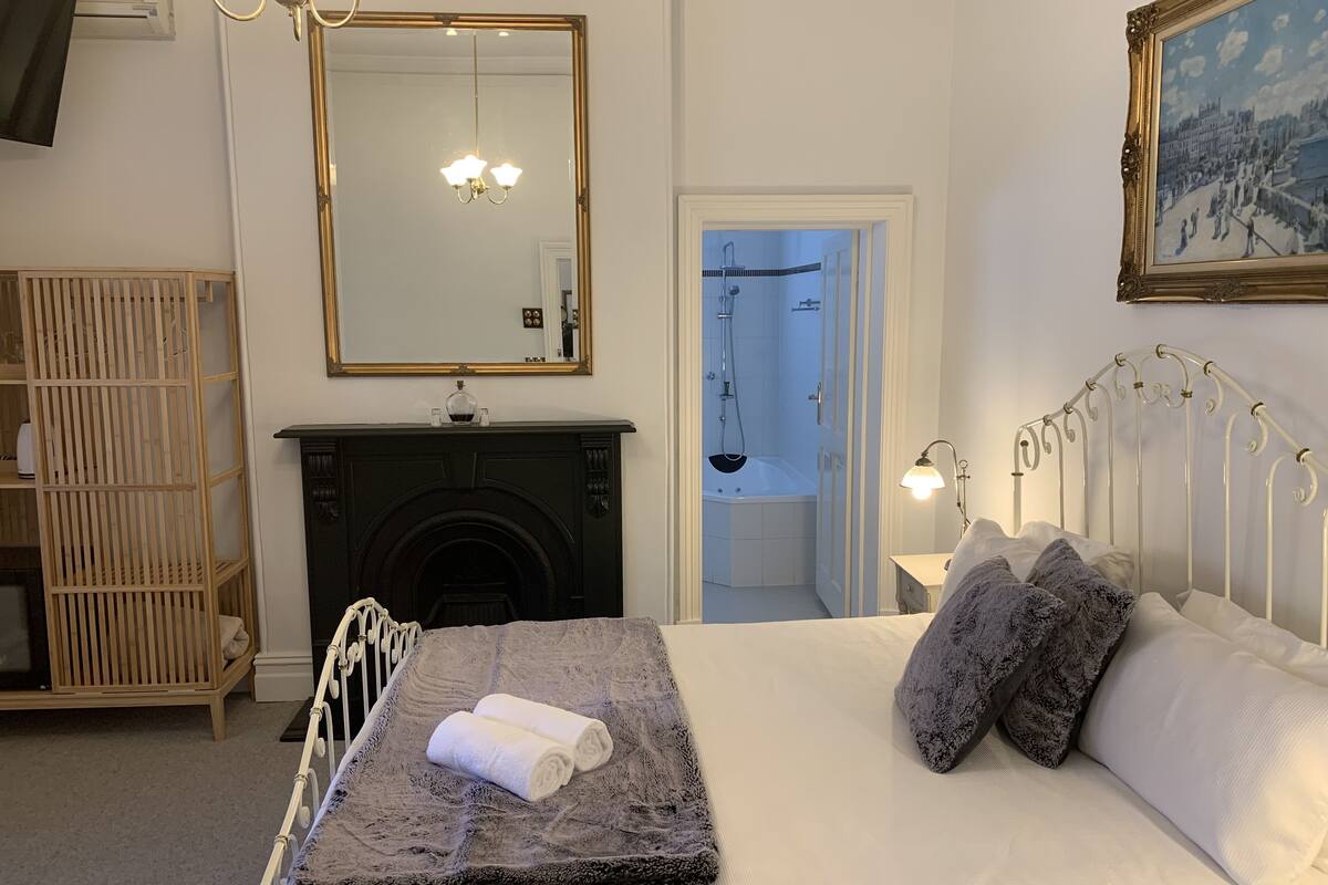 A bedroom with a bed, a fireplace, a mirror, and a painting.