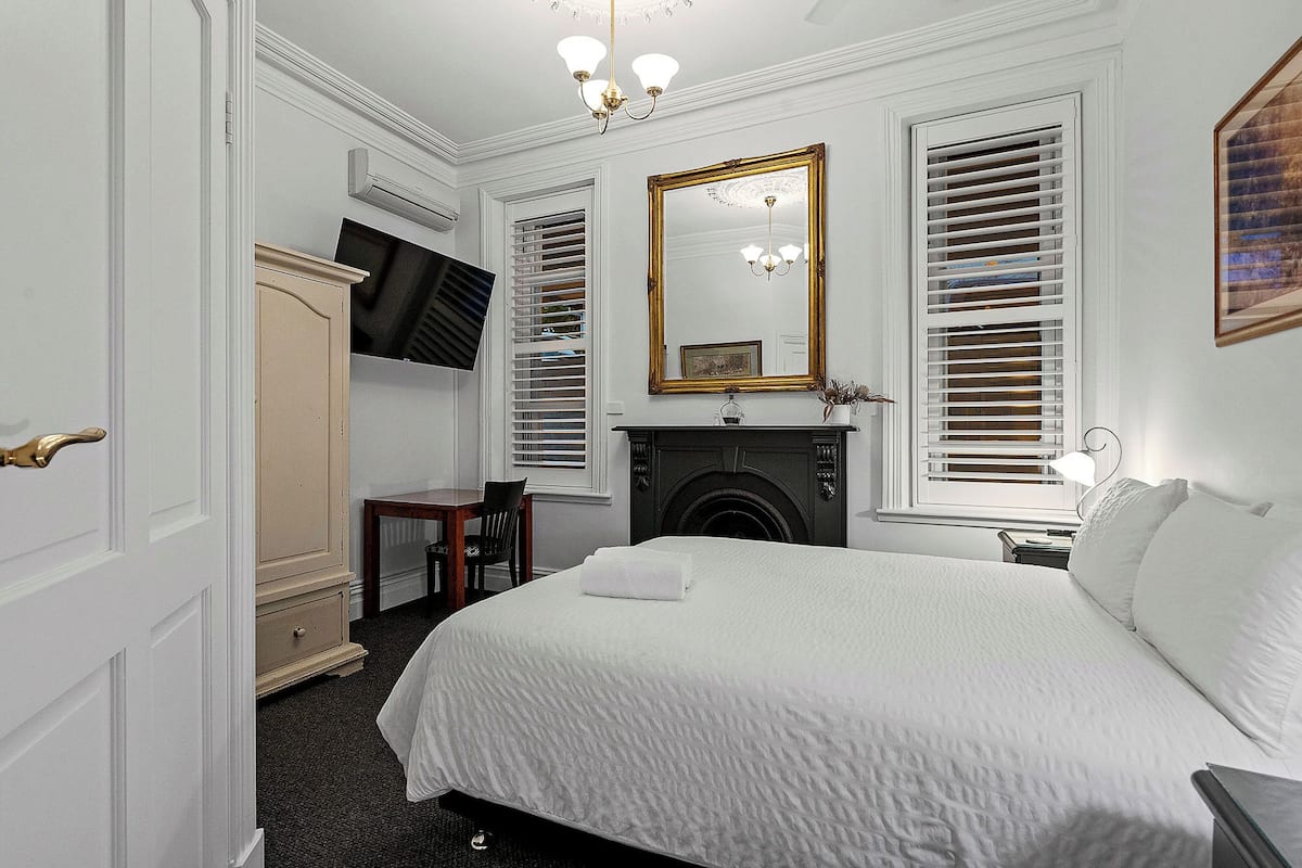 A bedroom with a bed, a dresser, a mirror, a fireplace, and a television.