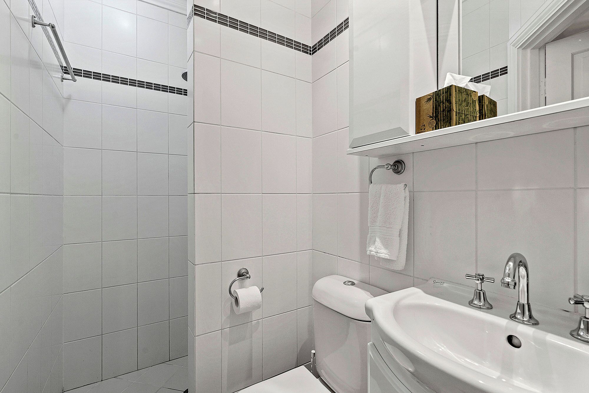 A bathroom with white tiles, a toilet, a sink with a mirror, and a towel rack.