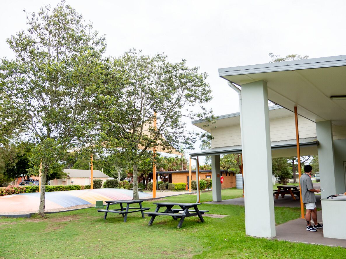 Un espace extérieur abrité avec des tables de pique-nique, une aire de jeux et un bâtiment à l’extérieur blanc.