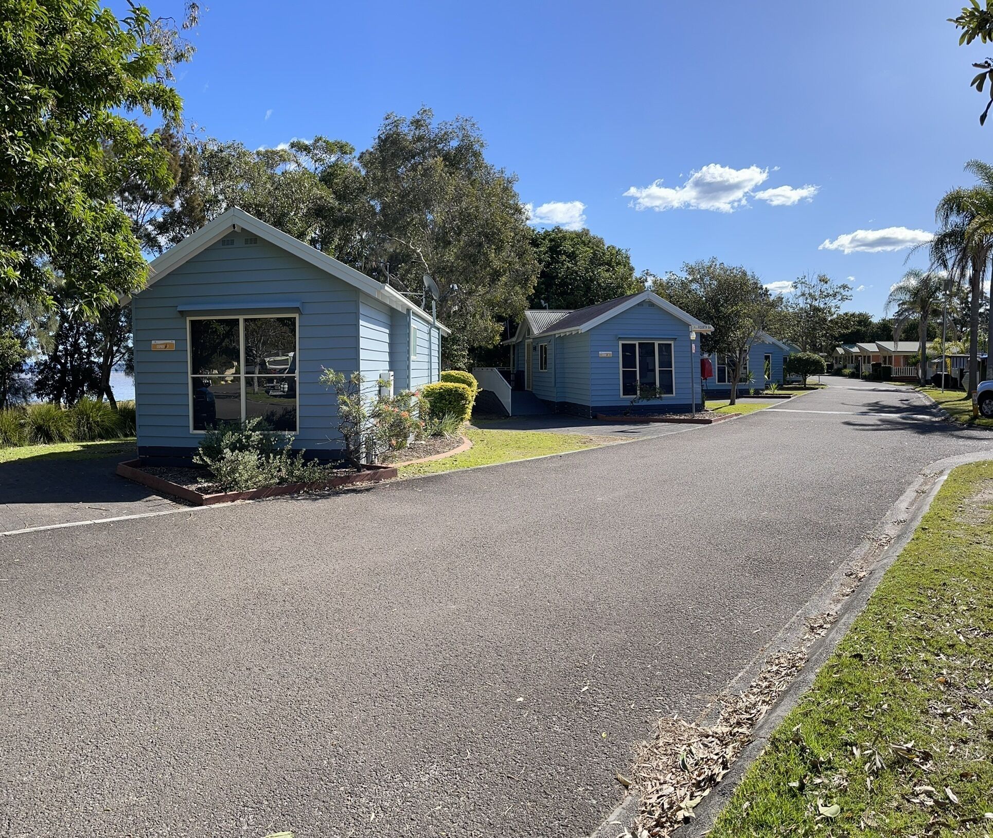 A row of small, blue, single-story buildings with a paved driveway and grassy areas.