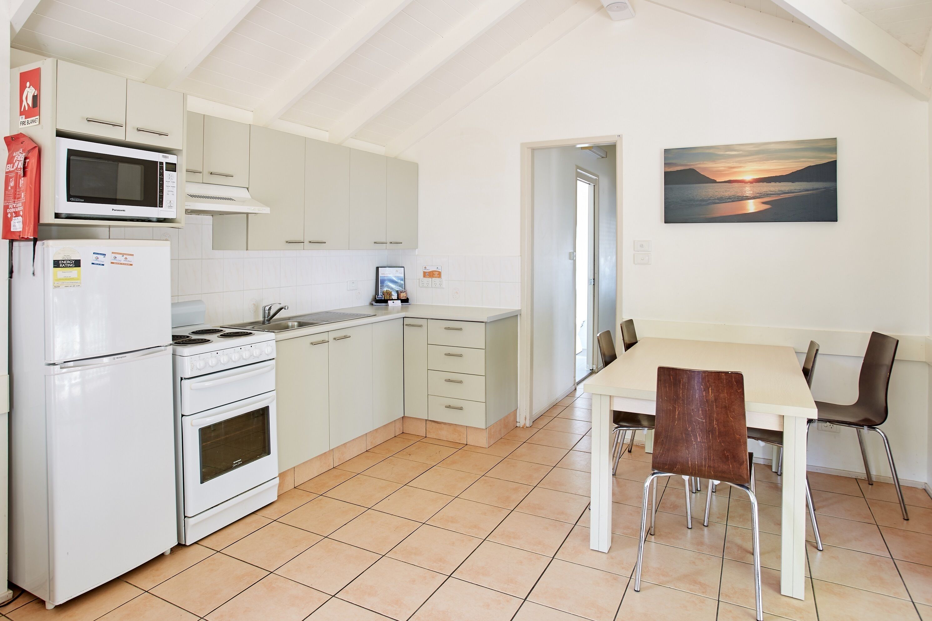 Een moderne keuken met witte apparaten, een eethoek met een tafel en stoelen, en een schilderij aan de muur.