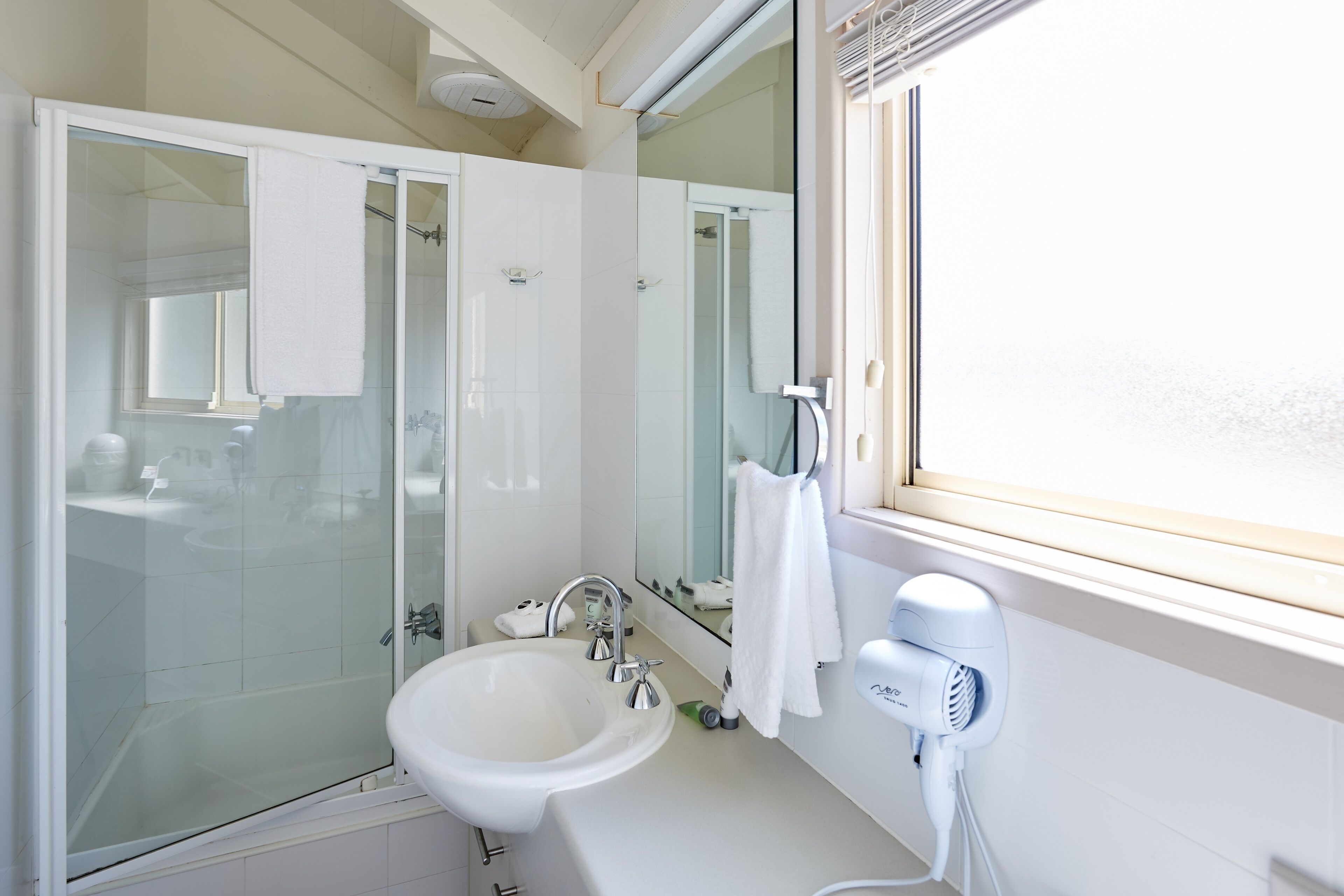 Ein modernes Badezimmer mit Duschkabine aus Glas, Waschbecken, Spiegel und Haartrockner.