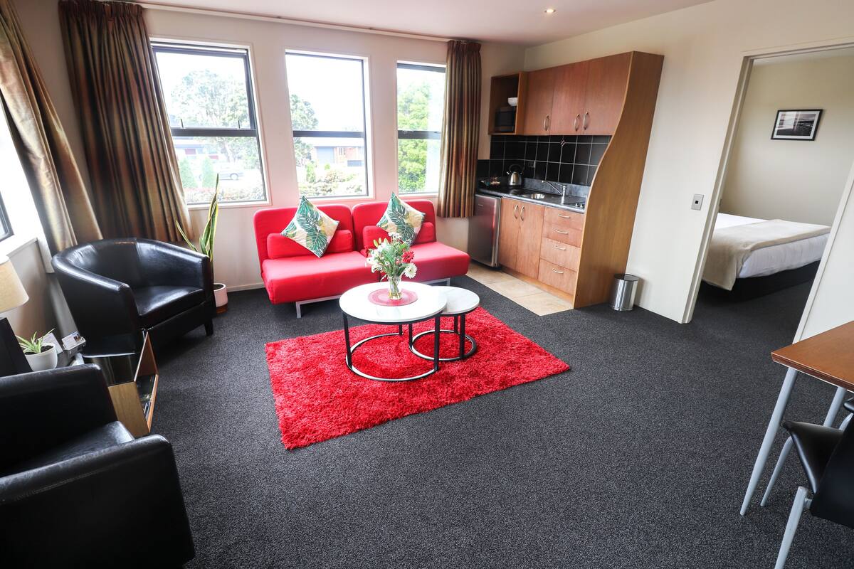 A compact living space with a red sofa, black chairs, a small round table, and a kitchenette.