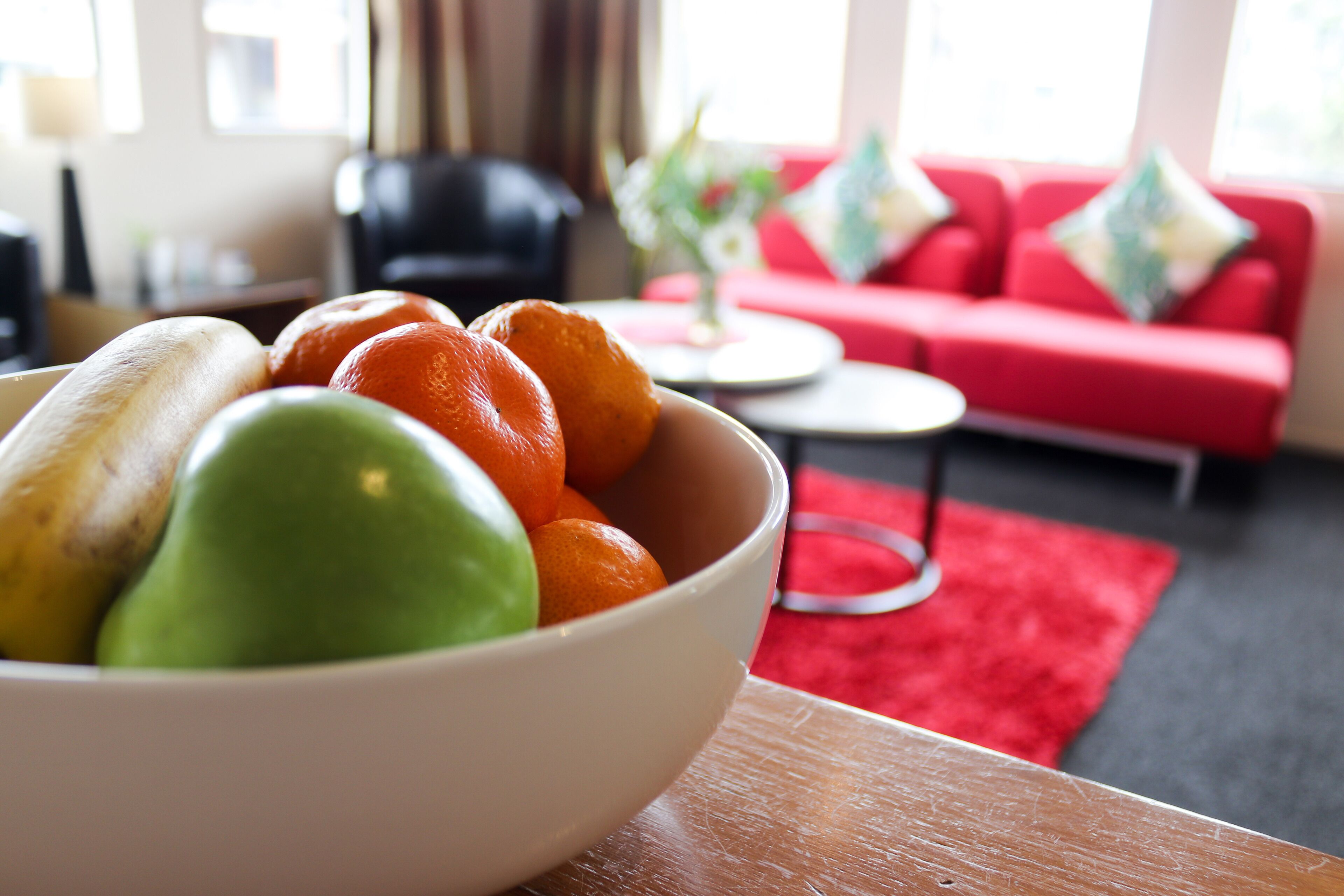 Un frutero con fruta sobre una mesa en una sala de estar con un sofá rojo y una mesa de centro.