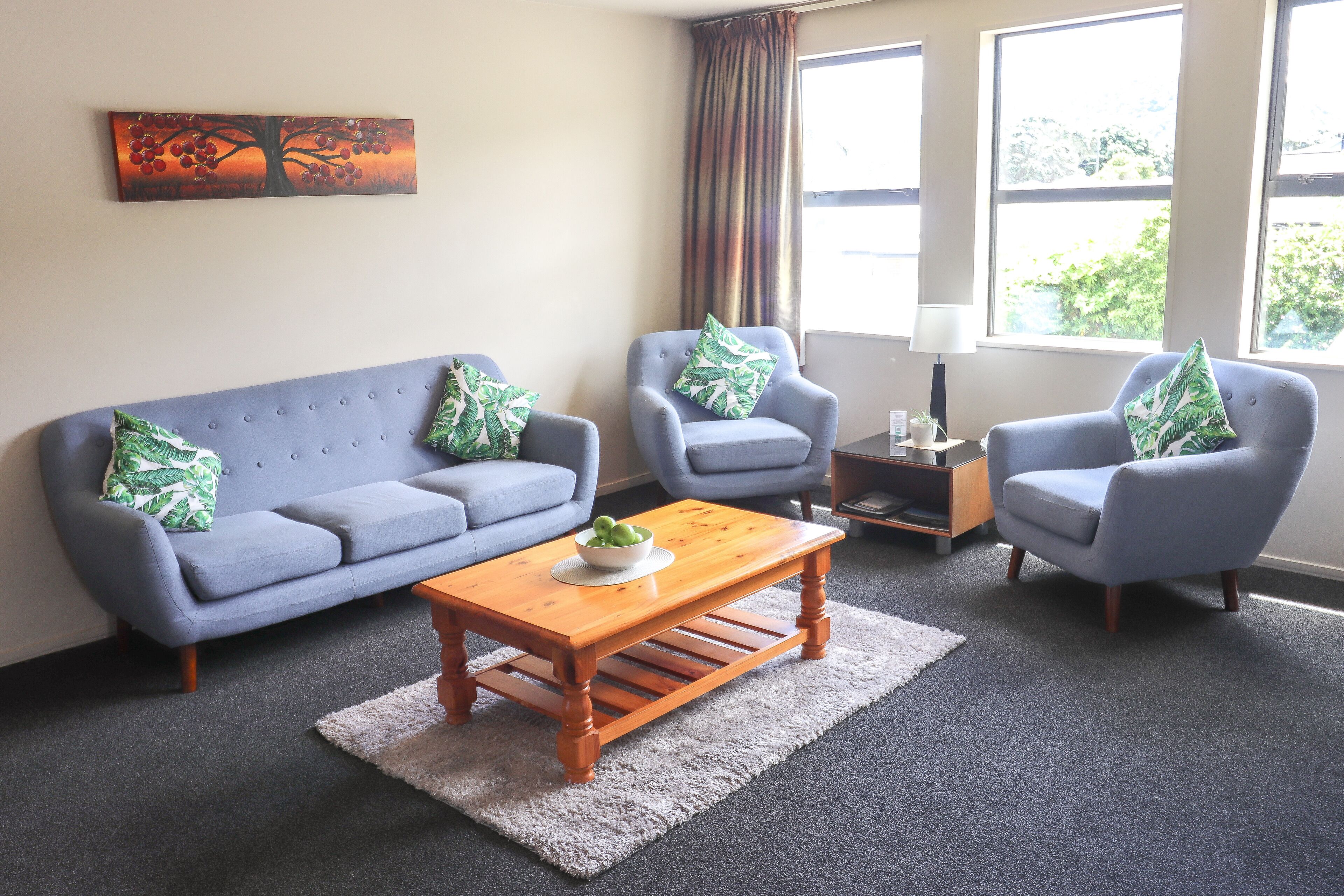 A living room with a grey sofa, two armchairs, a wooden coffee table, and a painting on the wall.