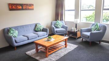 A living room with a grey sofa, two armchairs, a wooden coffee table, and a painting on the wall.