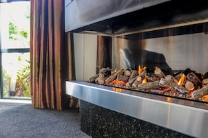 Una chimenea moderna con leña ardiendo, puerta de cristal y vista a la vegetación exterior.