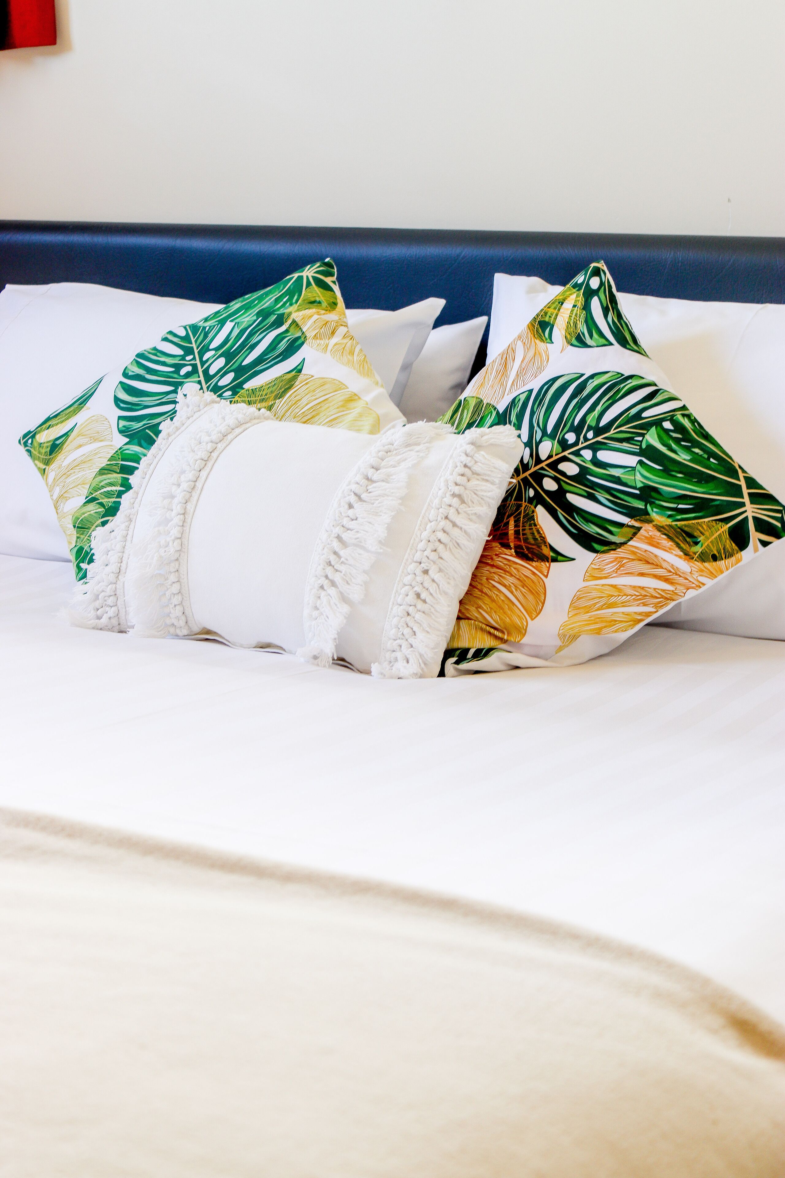 Un lit avec une literie blanche et des coussins décoratifs ornés de motifs de feuilles tropicales.